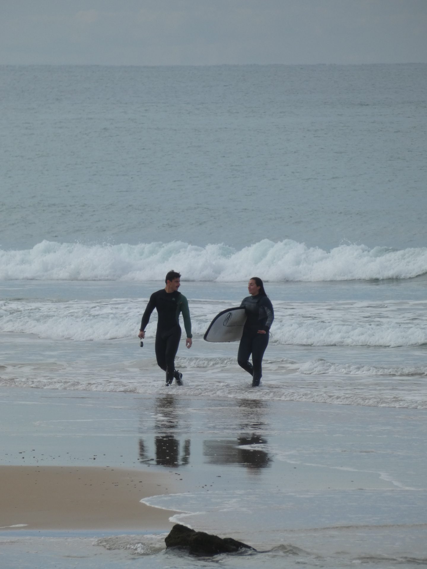 Dos surfistas con traje de neopreno caminando por la orilla en un día nublado tras surfear